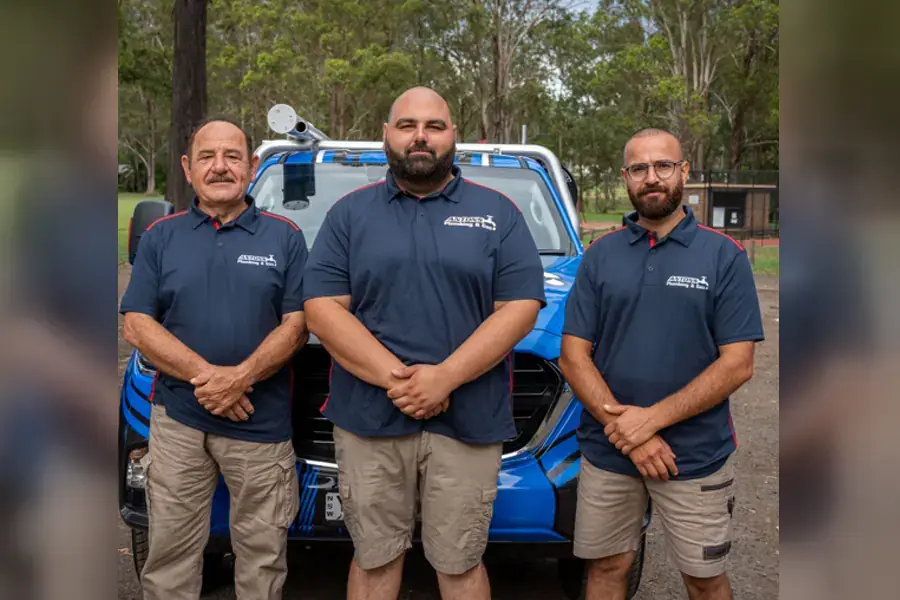 Three Antons plumbers standing beside a blue service vehicle